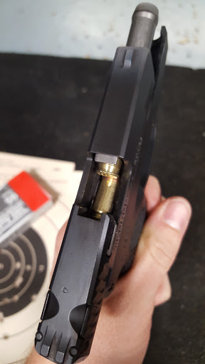 A hand checking the chamber of a semi-automatic pistol at the range, target visible in the background